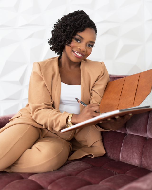 Christina Thompson seated on a sofa in a tan suit with a notebook